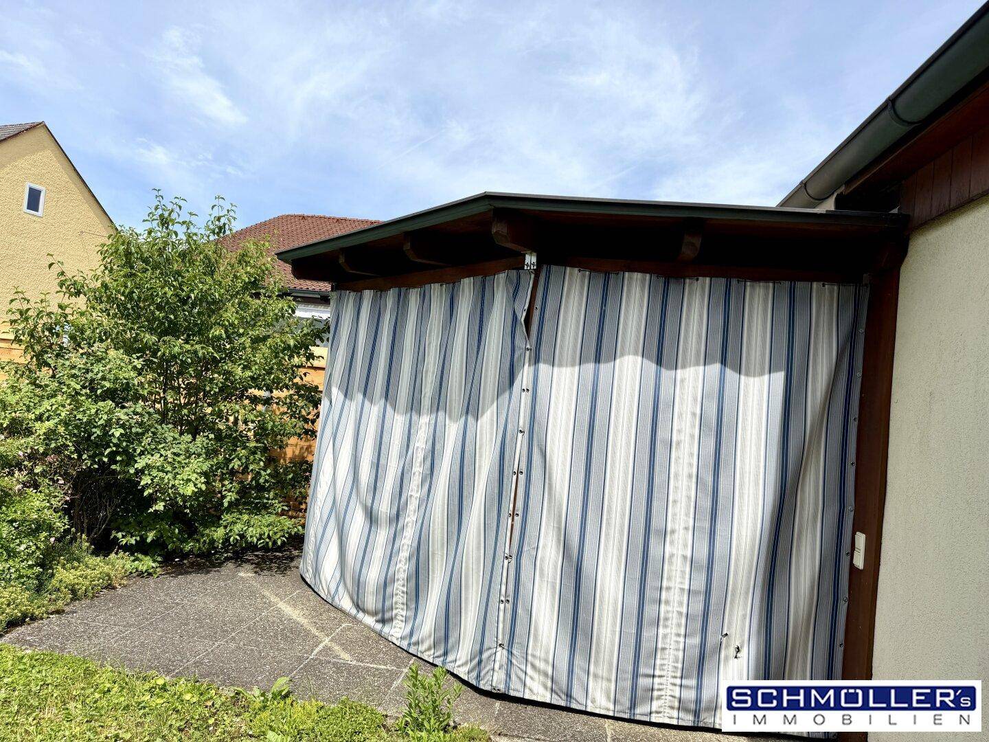 Gemütliche überdachte Terrasse mit blau-weiß gestreiften Vorhängen und Zugang zum Garten.