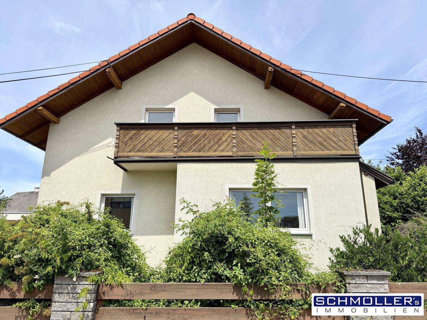 Detailansicht der Hausfassade mit Balkon und üppiger grüner Bepflanzung im Vorgarten.