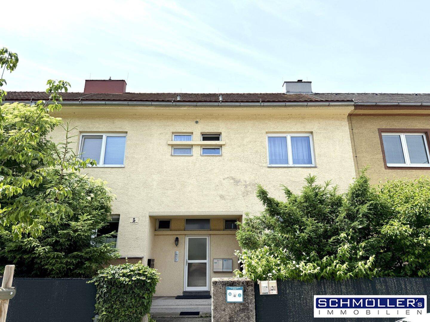 Frontansicht eines Reihenhauses mit gepflegter Fassade und grünen Büschen im Vorgartenbereich.