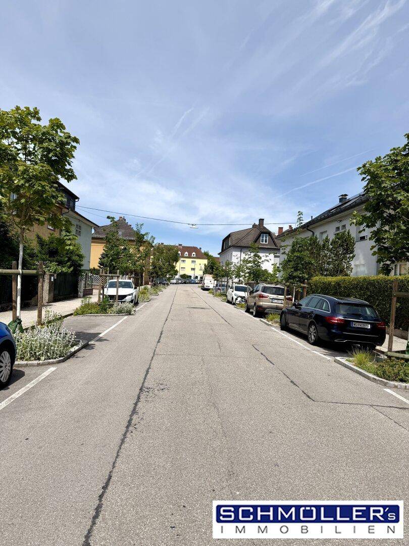 Ruhige Wohnstraße mit geparkten Autos und Bäumen entlang der Fahrbahn unter blauem Himmel.