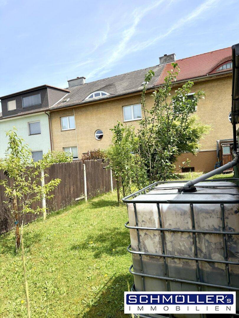 Grüner Gartenbereich mit jungen Bäumen und einem Wassertank hinter dem Reihenhaus.