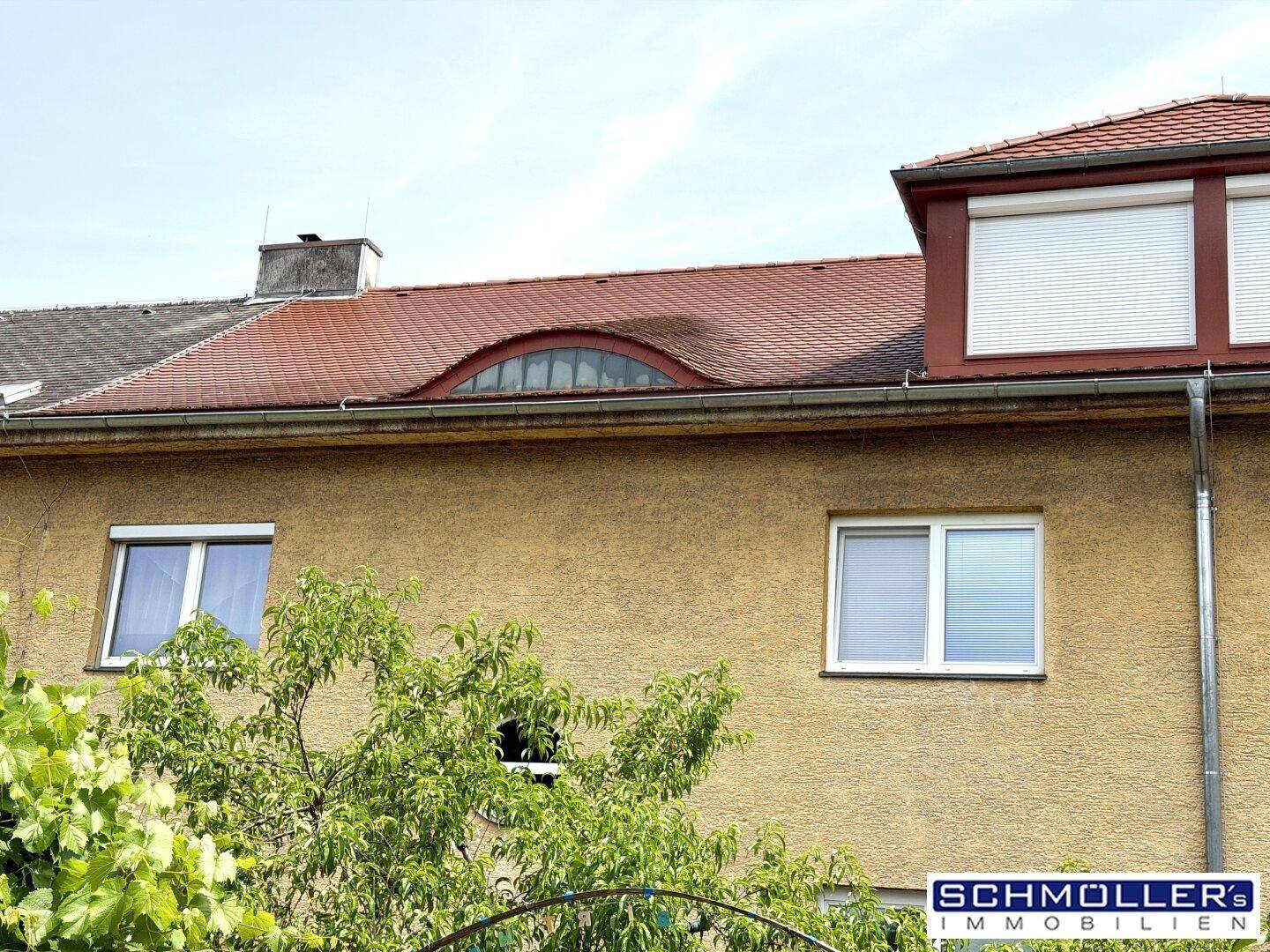 Rückansicht eines Reihenhauses mit Ziegeldach, Gaube und Rollläden an den Fenstern.