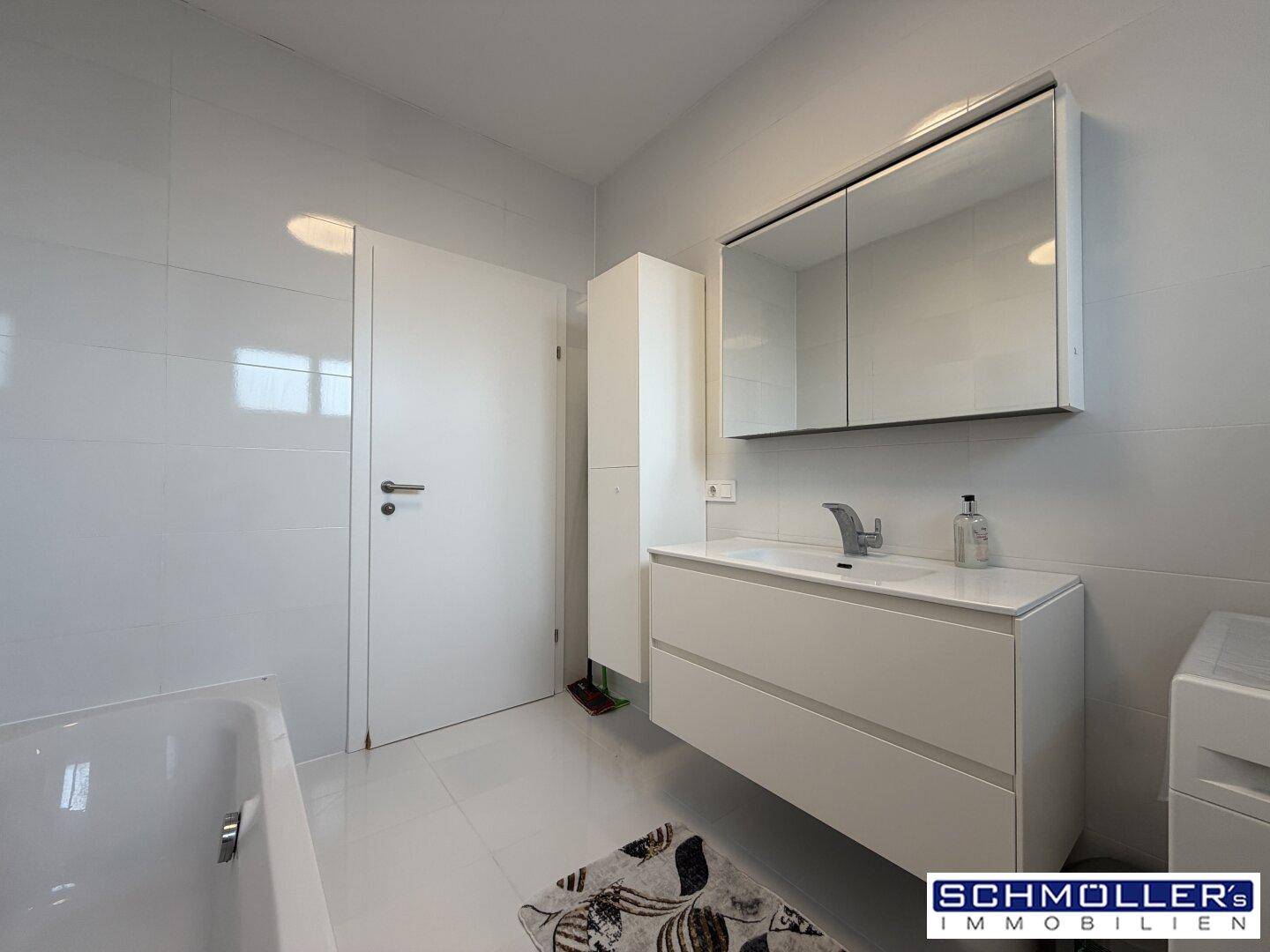 Helles Badezimmer mit Badewanne, Waschtisch und Spiegelschrank in Weiß.