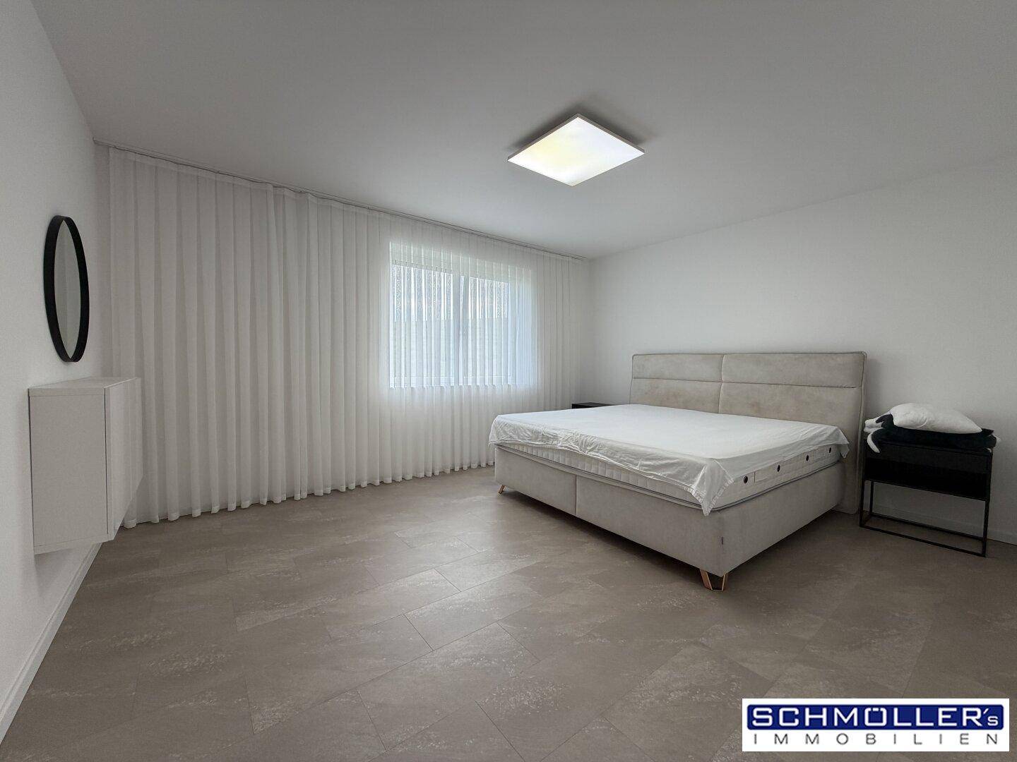 Helles Schlafzimmer mit großem Bett, weißen Vorhängen und modernem Fliesenboden.