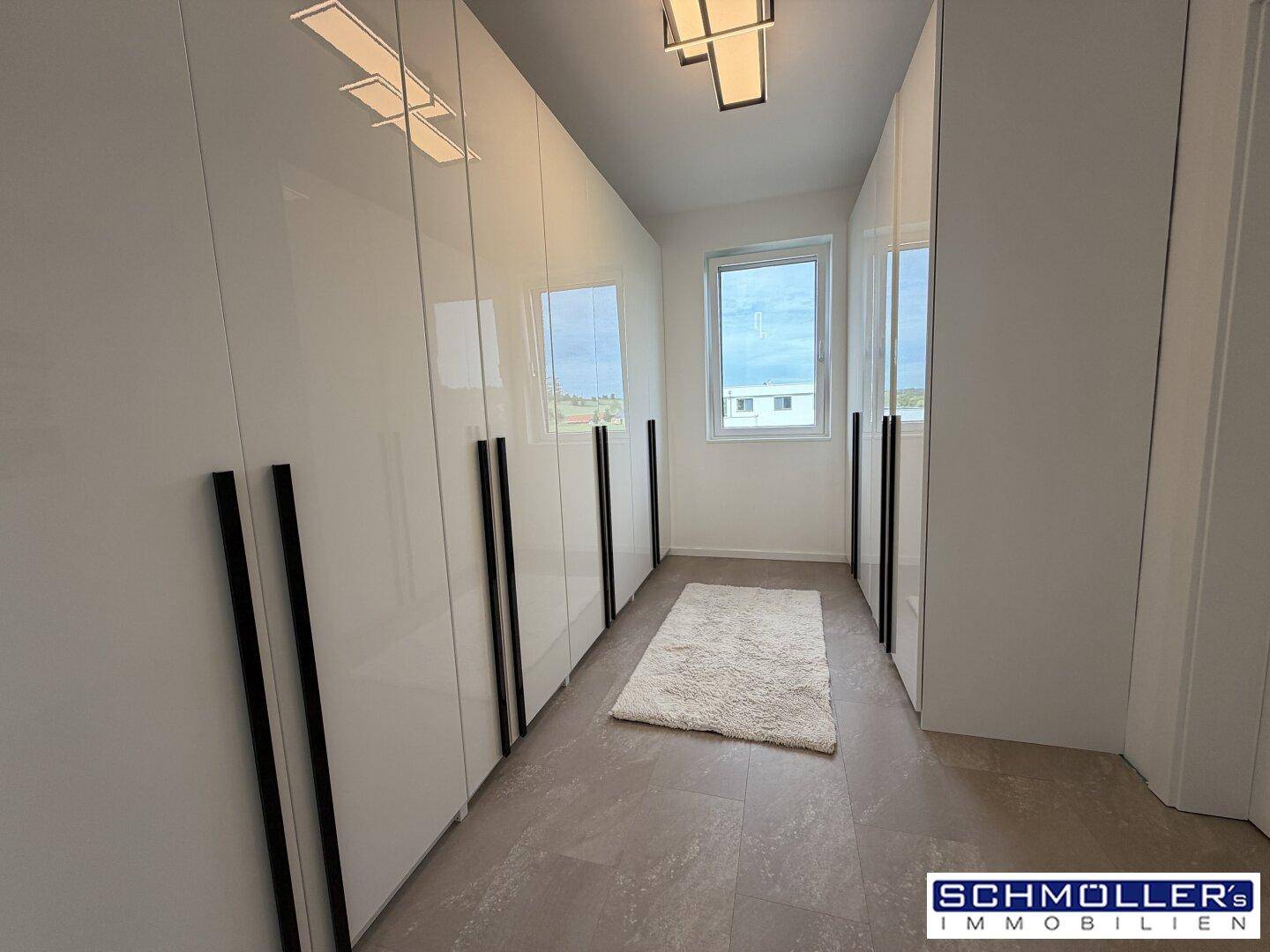 Geräumiger begehbarer Kleiderschrank mit weißen Hochglanzschränken und Fenster.