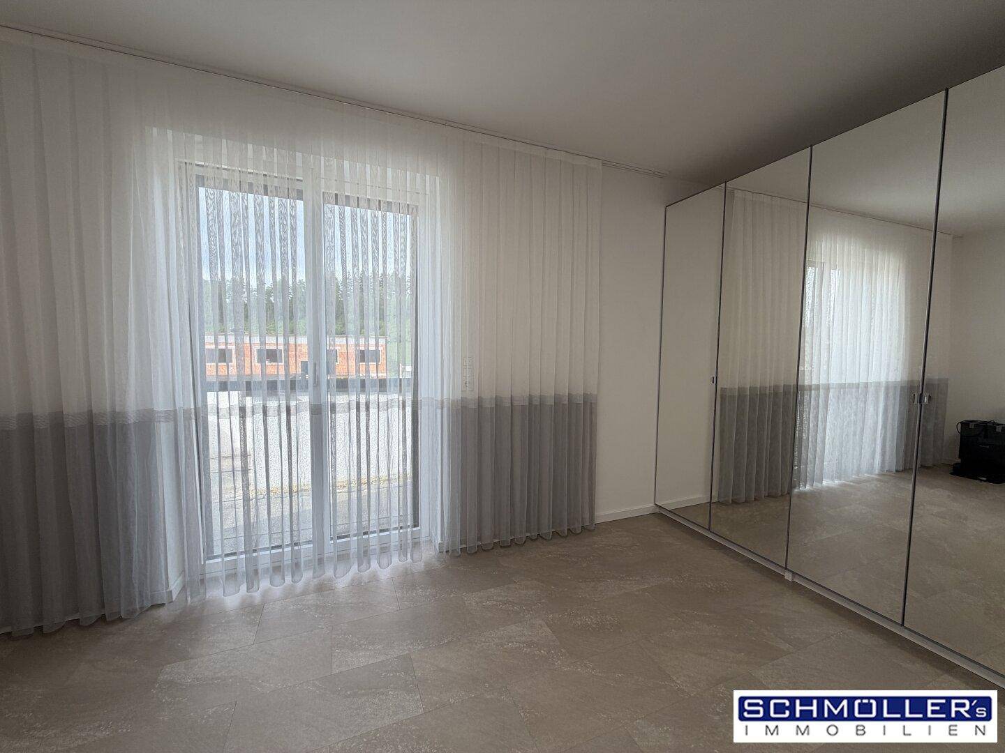 Schlafzimmer mit großem Spiegelschrank, Balkonzugang und hellen Vorhängen.