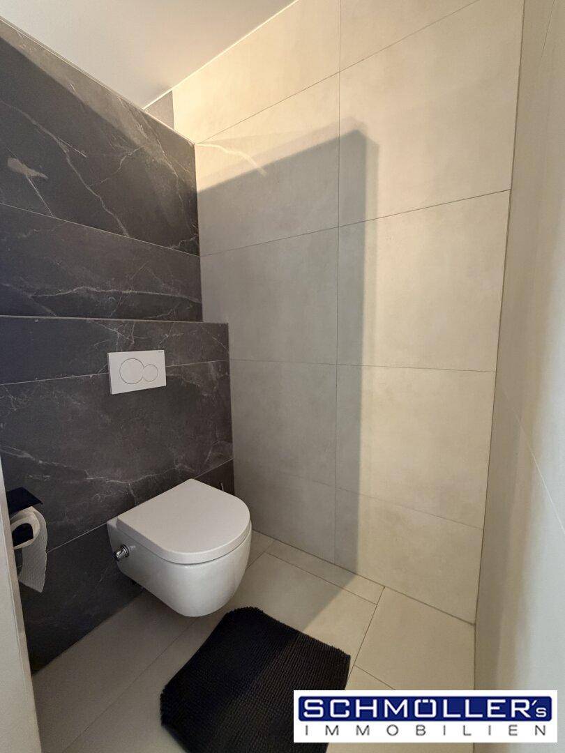 Wandhängendes WC in einem modernen Badezimmer mit grauen und weißen Fliesen.