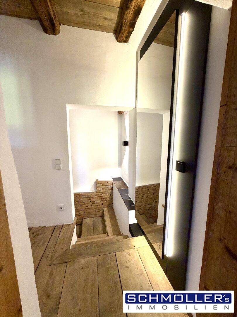 Rustikales Treppenhaus mit Holzbalken, modernen Spiegelelementen und weiß getünchten Wänden.