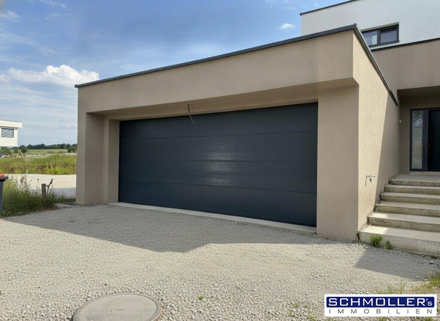 Moderne Doppelgarage mit dunklem Tor und Kiesauffahrt vor dem Haus.