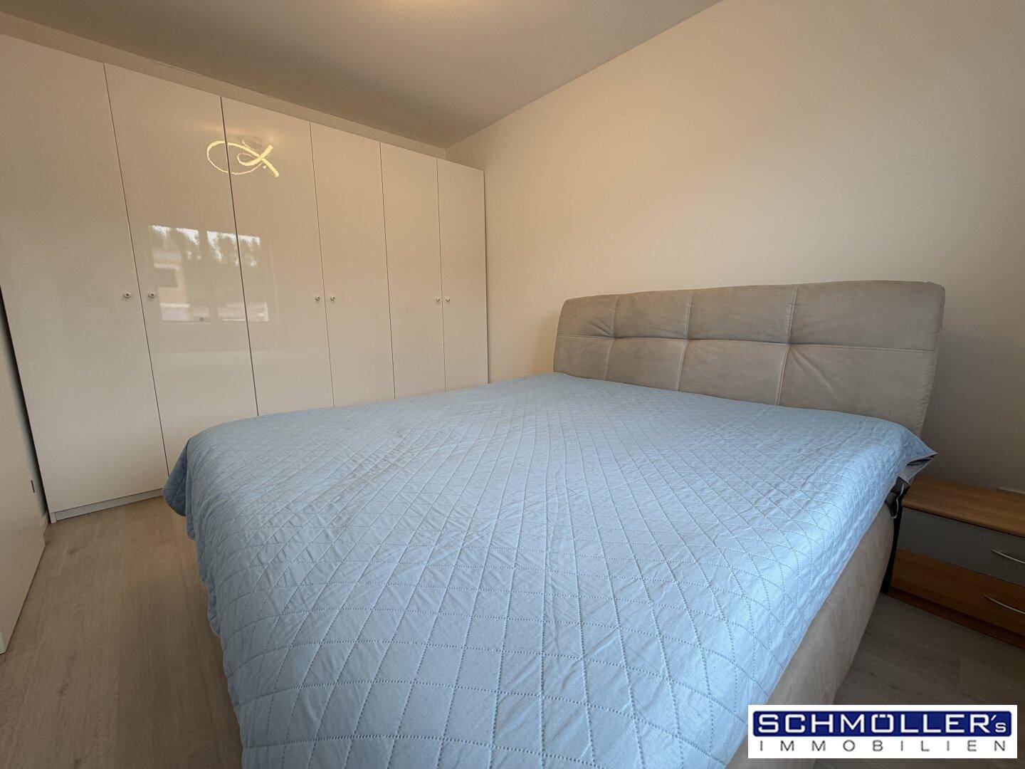 Schlafzimmer mit großem Bett, weißen Einbauschränken und hellem Laminatboden.