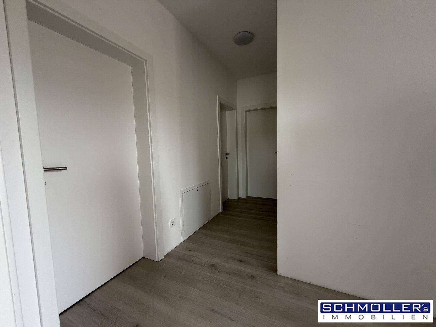 Schlichter Flur mit weißen Türen und hellem Laminatboden, der zu weiteren Räumen führt.
