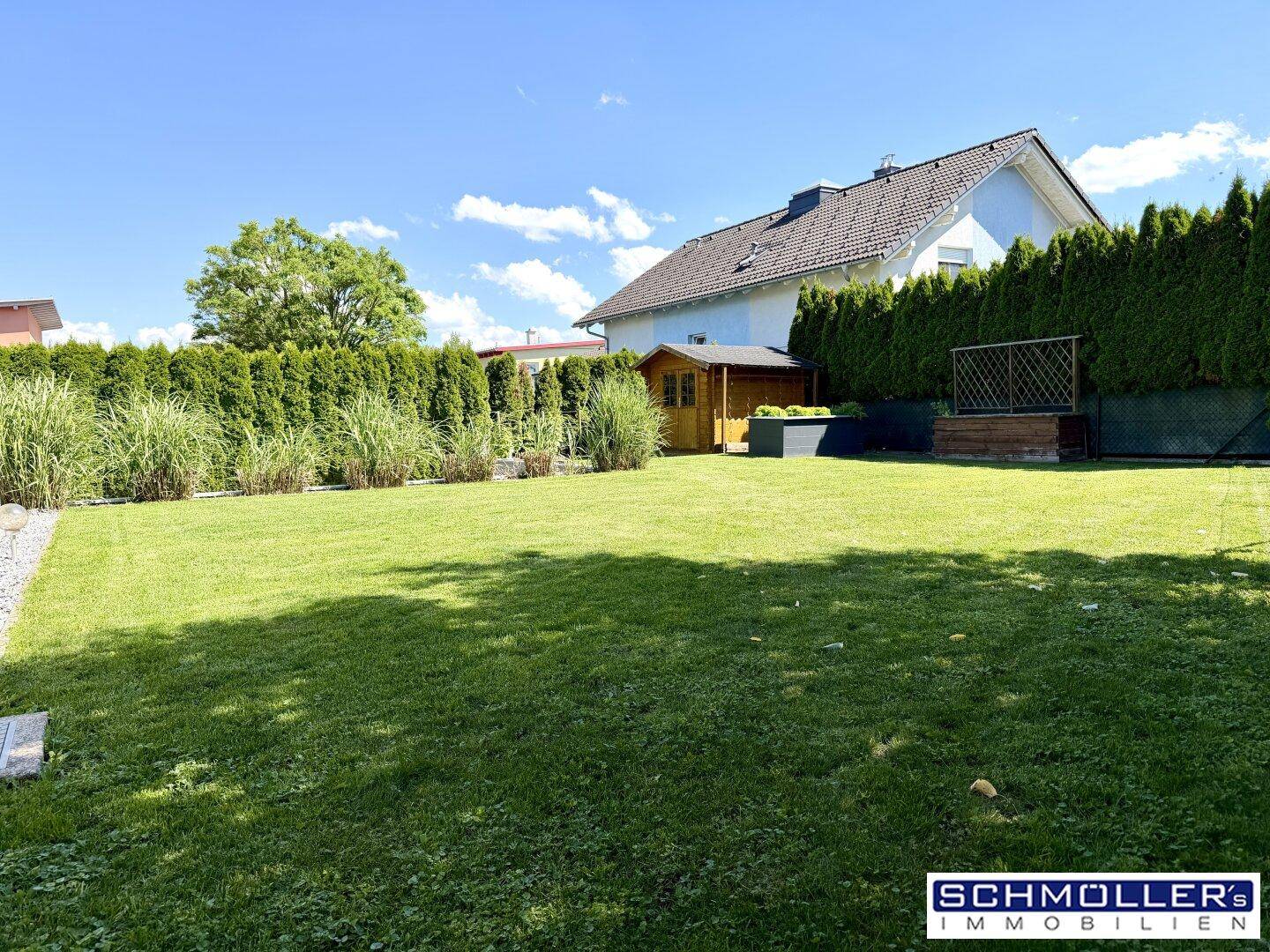 Gepflegter Garten mit Rasenfläche, hoher Hecke und einem kleinen Holzschuppen im Hintergrund.