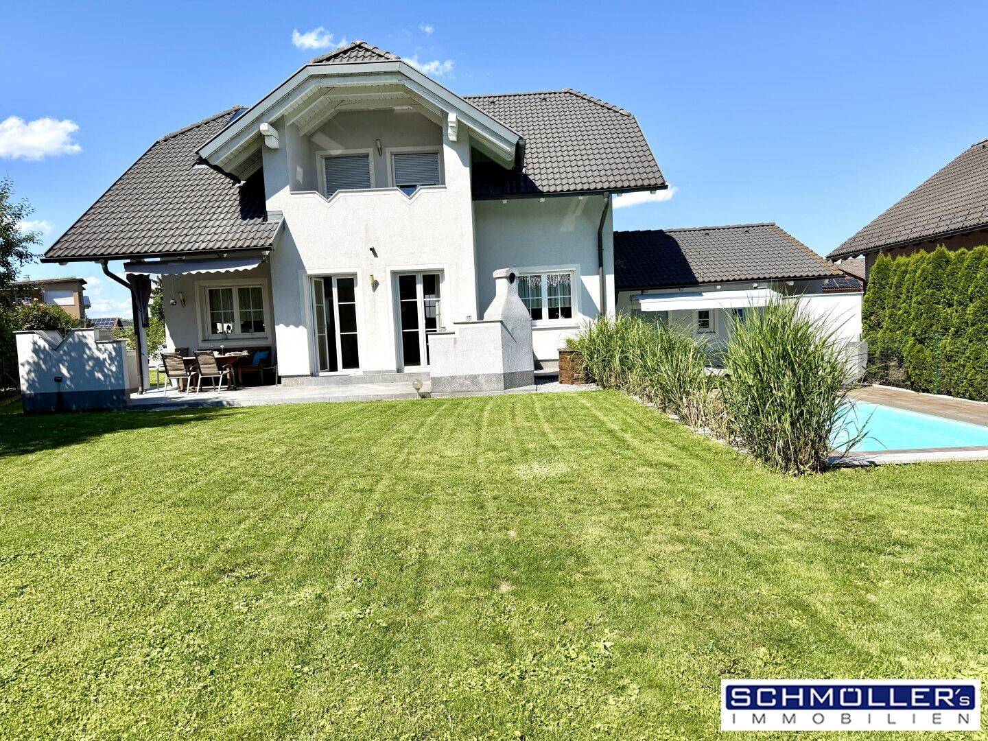 Weitläufiger Gartenbereich mit Rasenfläche, Pool und dem modernen Einfamilienhaus im Hintergrund.