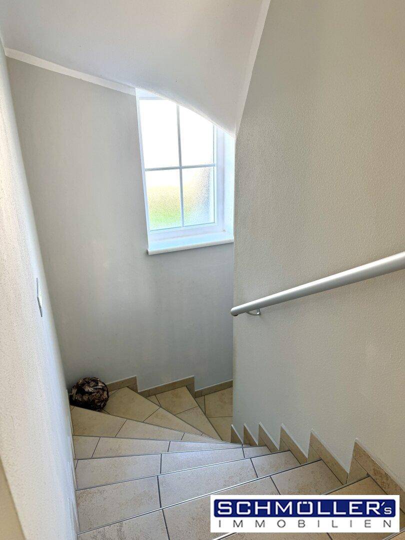 Helle Treppe mit Fliesenstufen und Handlauf, die zu einer weiteren Etage führt.