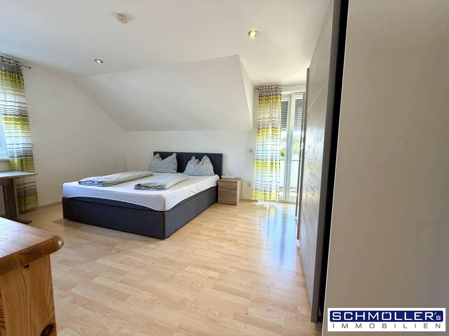 Helles Schlafzimmer mit Holzboden, Dachschräge und Zugang zu einem französischen Balkon.