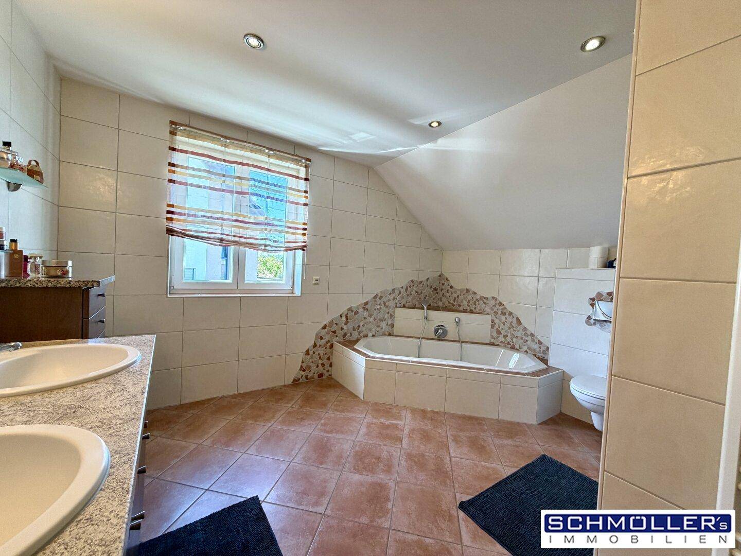 Großes Badezimmer mit Doppelwaschbecken, Eckbadewanne und Fenster unter der Dachschräge.