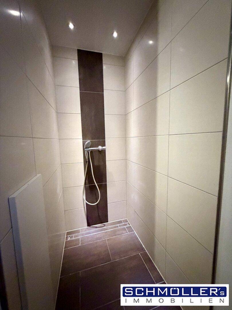 Moderne Duschkabine mit dunklen Akzentfliesen und bodengleichem Zugang.