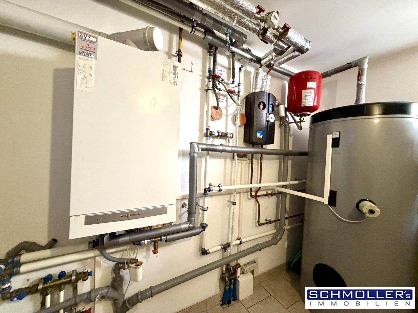 Technikraum mit Heizungsanlage, Warmwasserspeicher und sichtbaren Rohrleitungen.