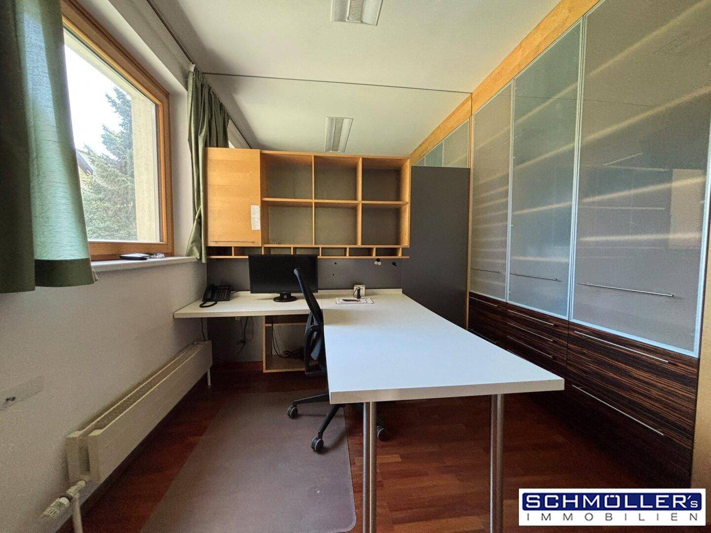 Arbeitszimmer mit Schreibtisch, Computer und integrierten Regalen, Holzboden und Fensterblick.