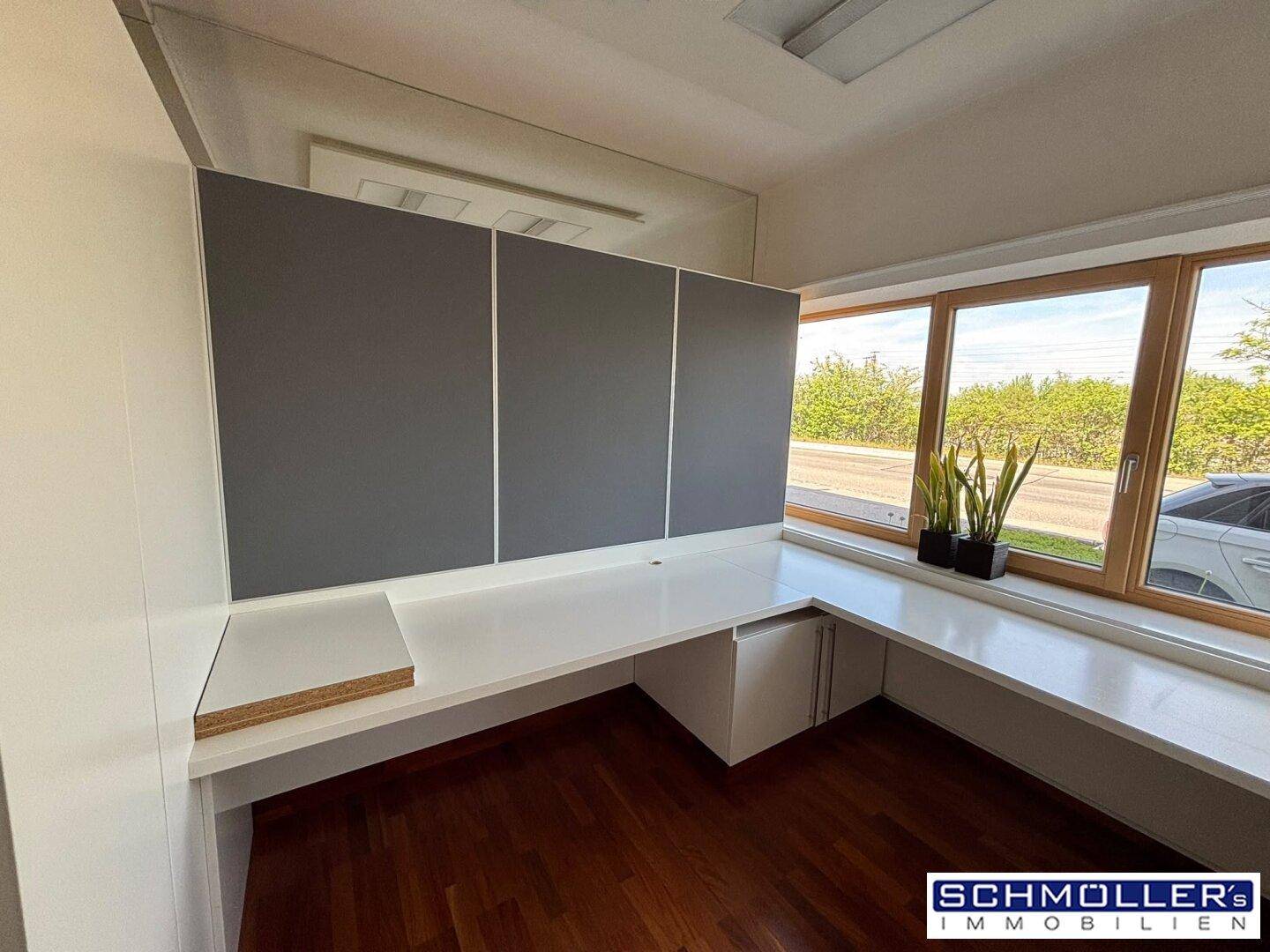 Büroecke mit integriertem Schreibtisch, grauen Akustikpaneelen, Holzboden und weitem Ausblick.