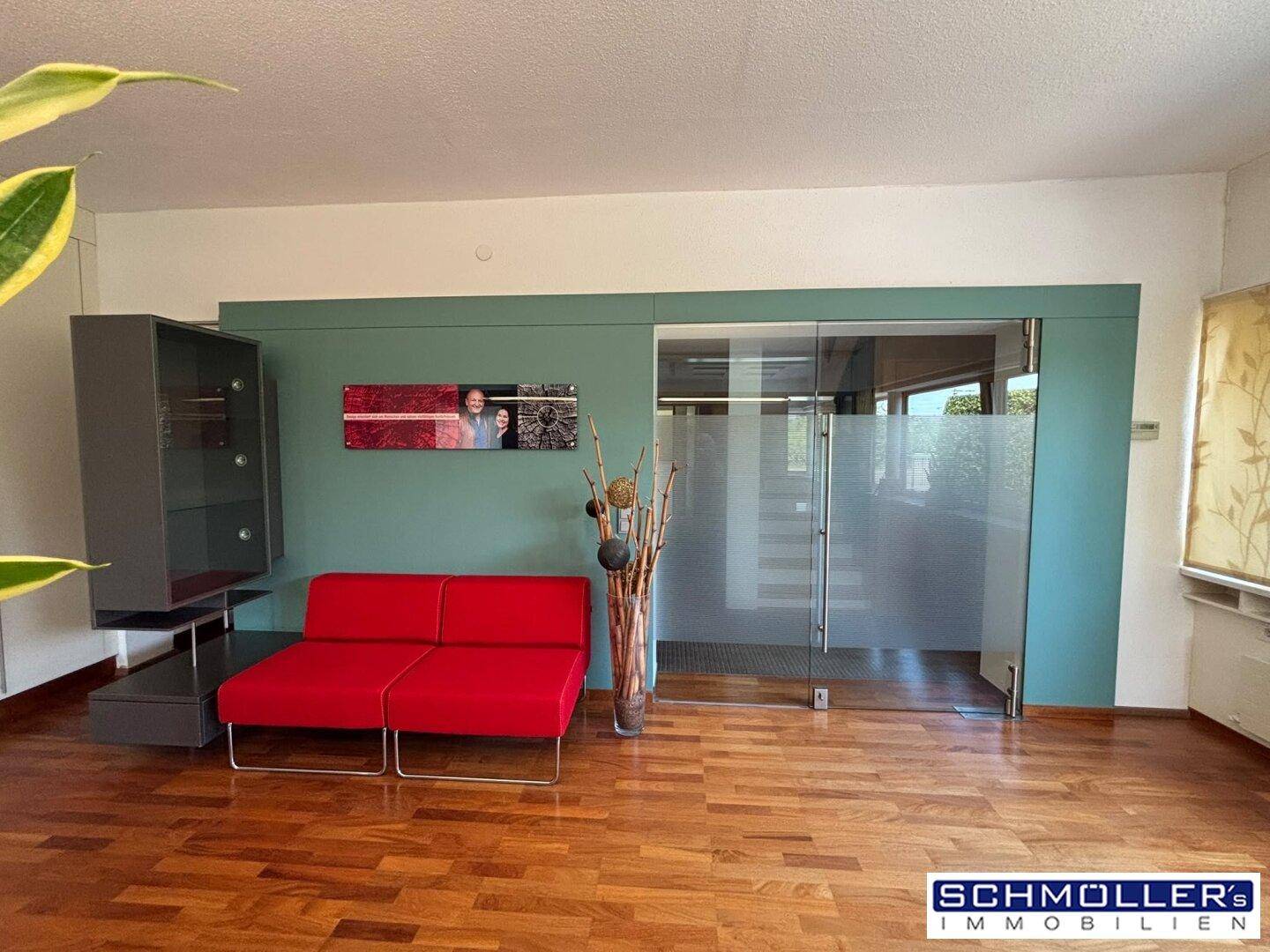 Wartebereich oder Lounge mit rotem Sofa, Holzboden und einer modernen Schiebetür aus Milchglas.