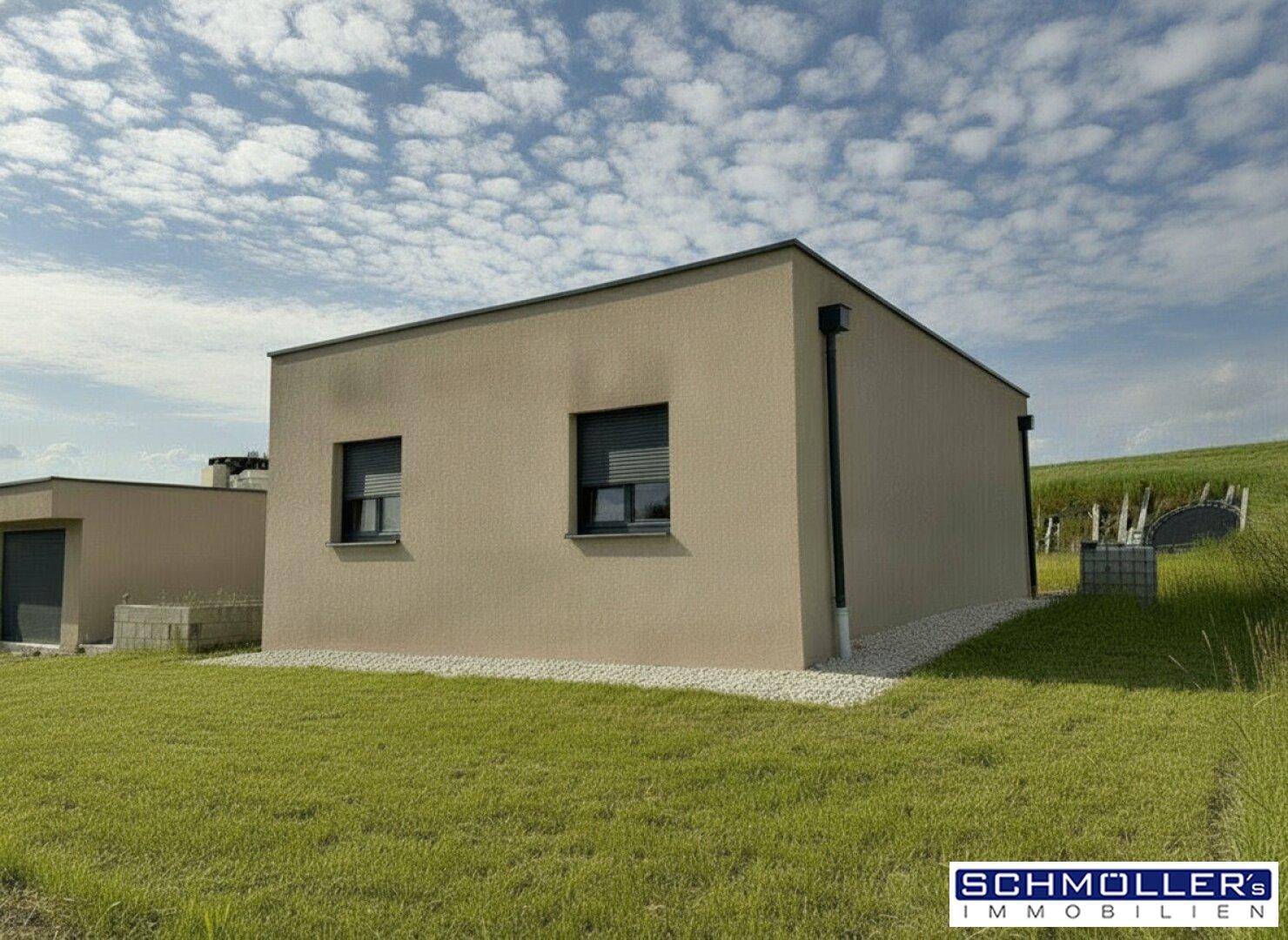Seitliche Ansicht eines modernen Gebäudes mit beiger Fassade und flachem Dach, umgeben von Grünflächen.