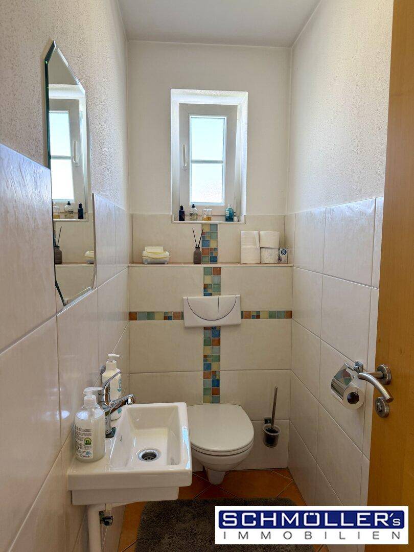 Kleines Gäste-WC mit Fenster, wandhängendem WC und farbigen Fliesenakzenten.