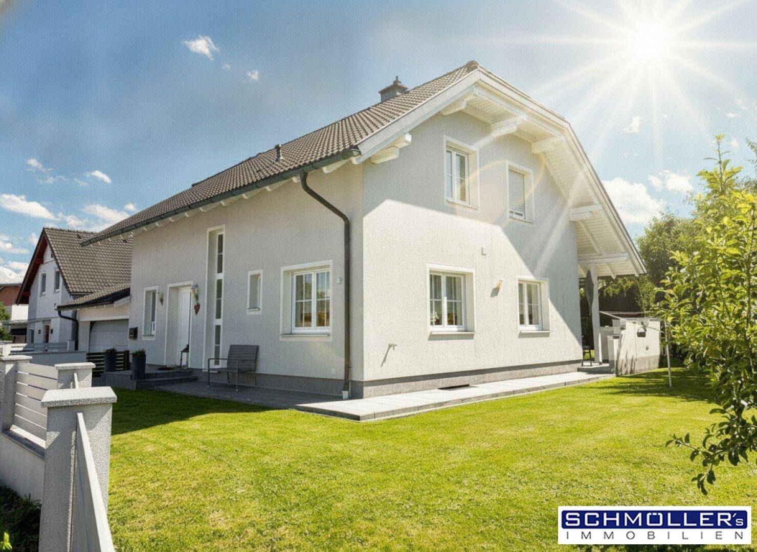 Seitenansicht des modernen Einfamilienhauses mit weißer Fassade und gepflegtem Vorgarten bei Sonnenschein.