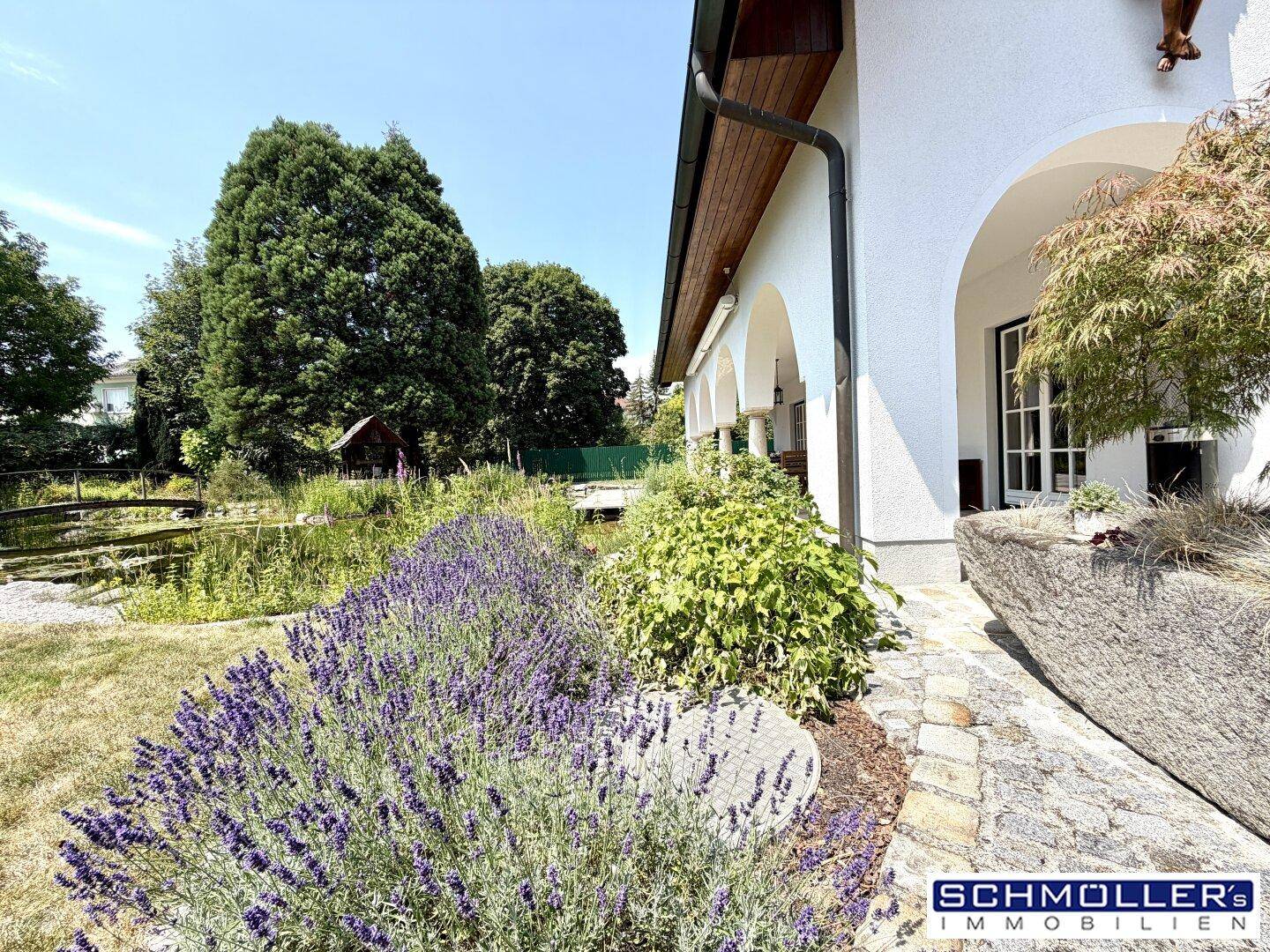 Seitenansicht des Hauses mit blühendem Lavendel, Steinweg und Blick auf den Teich.
