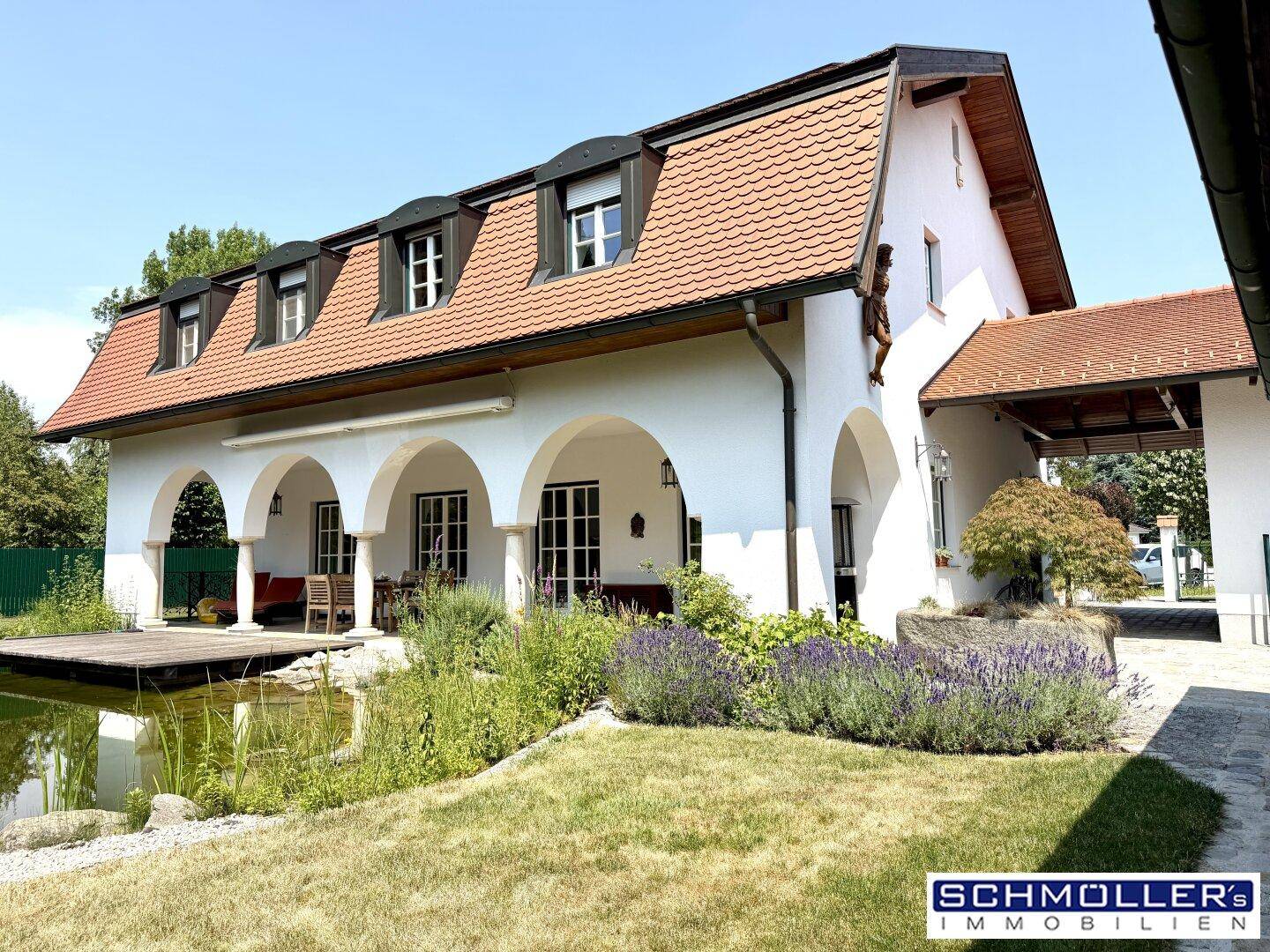 Großzügiges Haus mit traditioneller Architektur, überdachter Loggia, Teich und gepflegtem Gartenbereich.