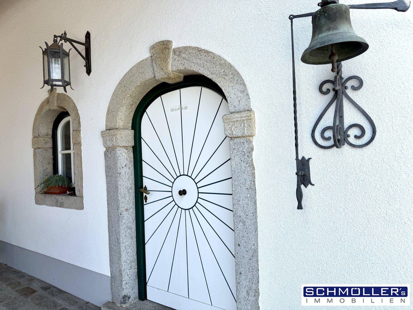 Traditioneller Hauseingang mit kunstvoller Holztür, Steinbogen und historischer Glocke.