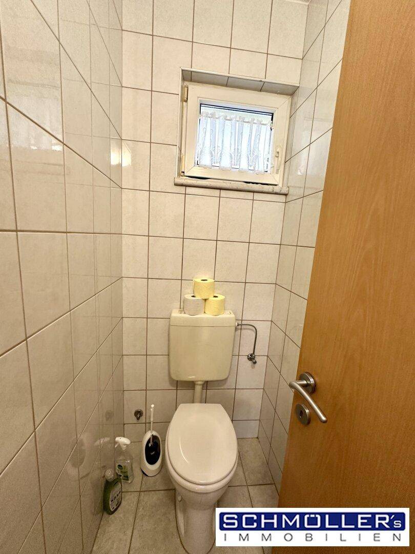 Kleines separates WC mit weißen Fliesen, Toilette und einem Fenster für Tageslicht.