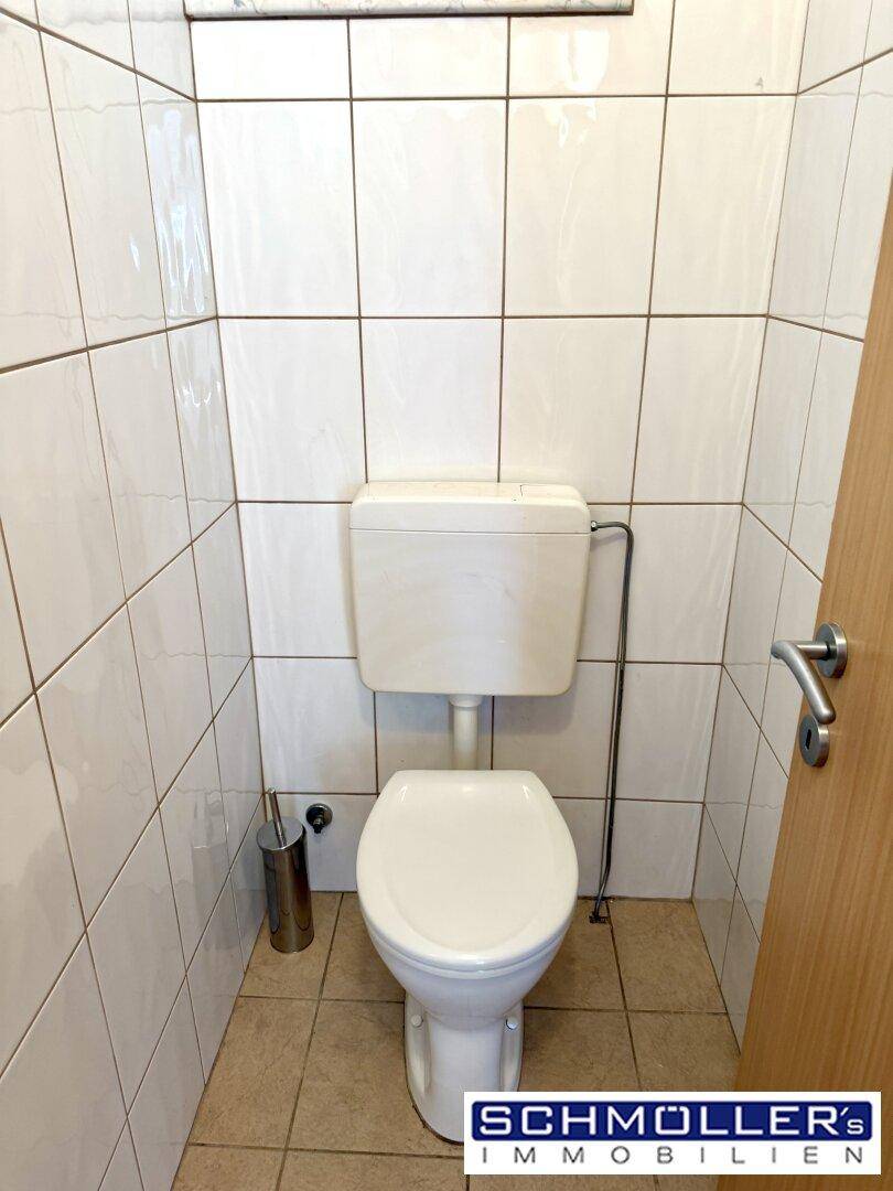 Einfaches separates WC mit weißen Fliesen und Toilette, funktional und sauber.