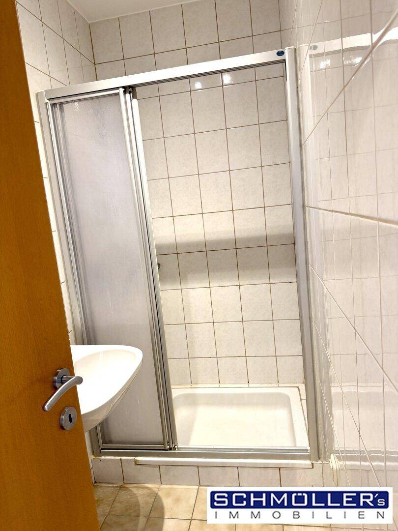 Gefliestes Badezimmer mit Duschkabine und kleinem Waschbecken, in gutem Zustand.
