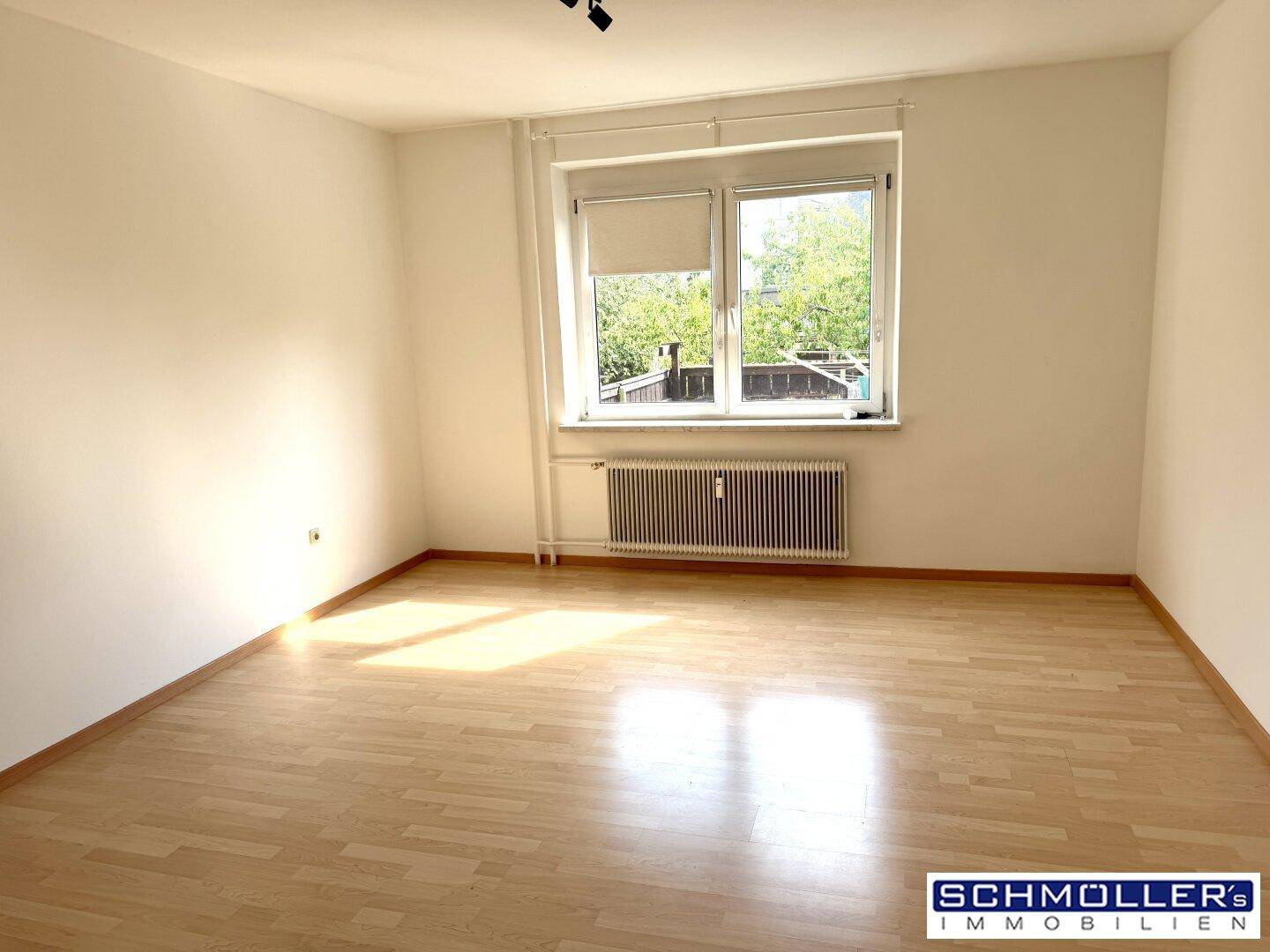 Heller, leerer Raum mit Laminatboden, großen Fenstern und viel natürlichem Tageslicht.