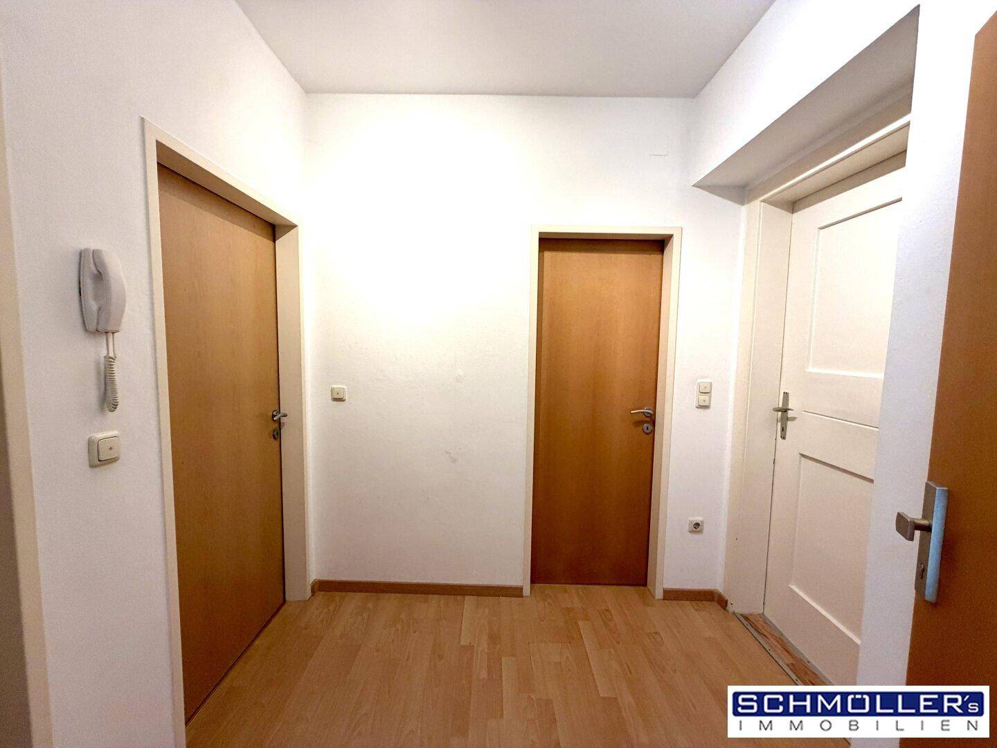 Heller Flur mit Laminatboden und mehreren Holztüren, der verschiedene Räume verbindet.