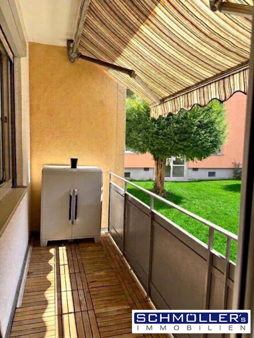 Sonniger Balkon mit Holzbodenfliesen und direktem Blick auf die grüne Gartenanlage.