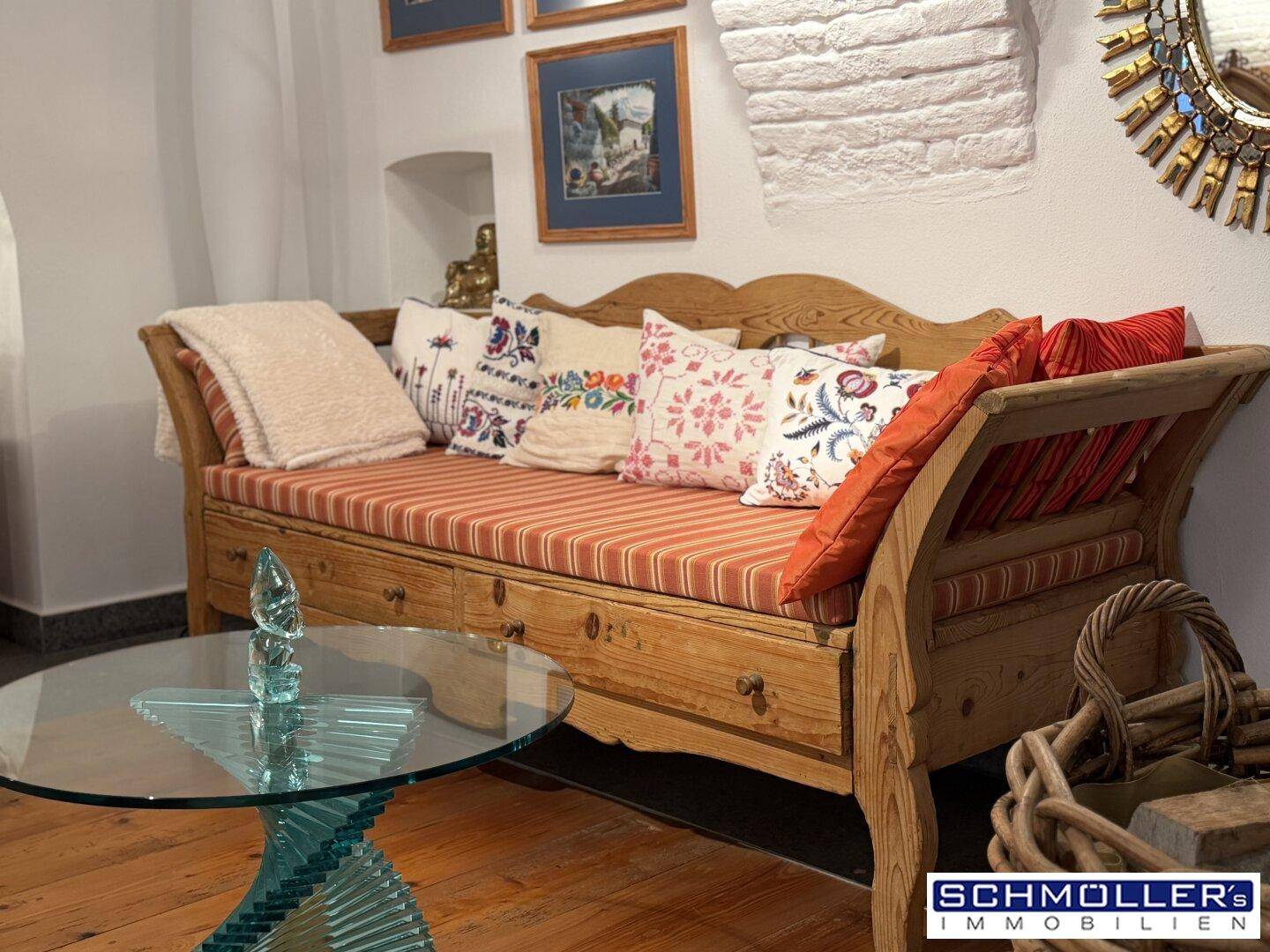 Gemütliche Holzliege mit bunten Kissen und einem modernen Glastisch im Wohnbereich.