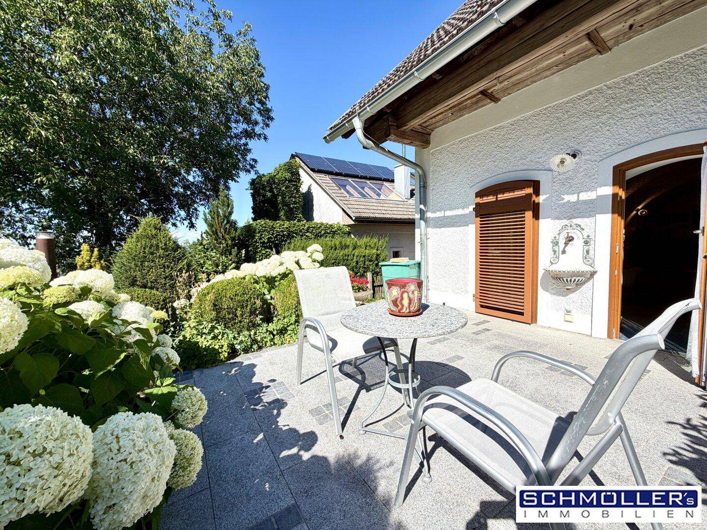 Kleine, sonnige Terrasse mit Sitzgelegenheiten und blühenden Hortensien im Vordergrund.