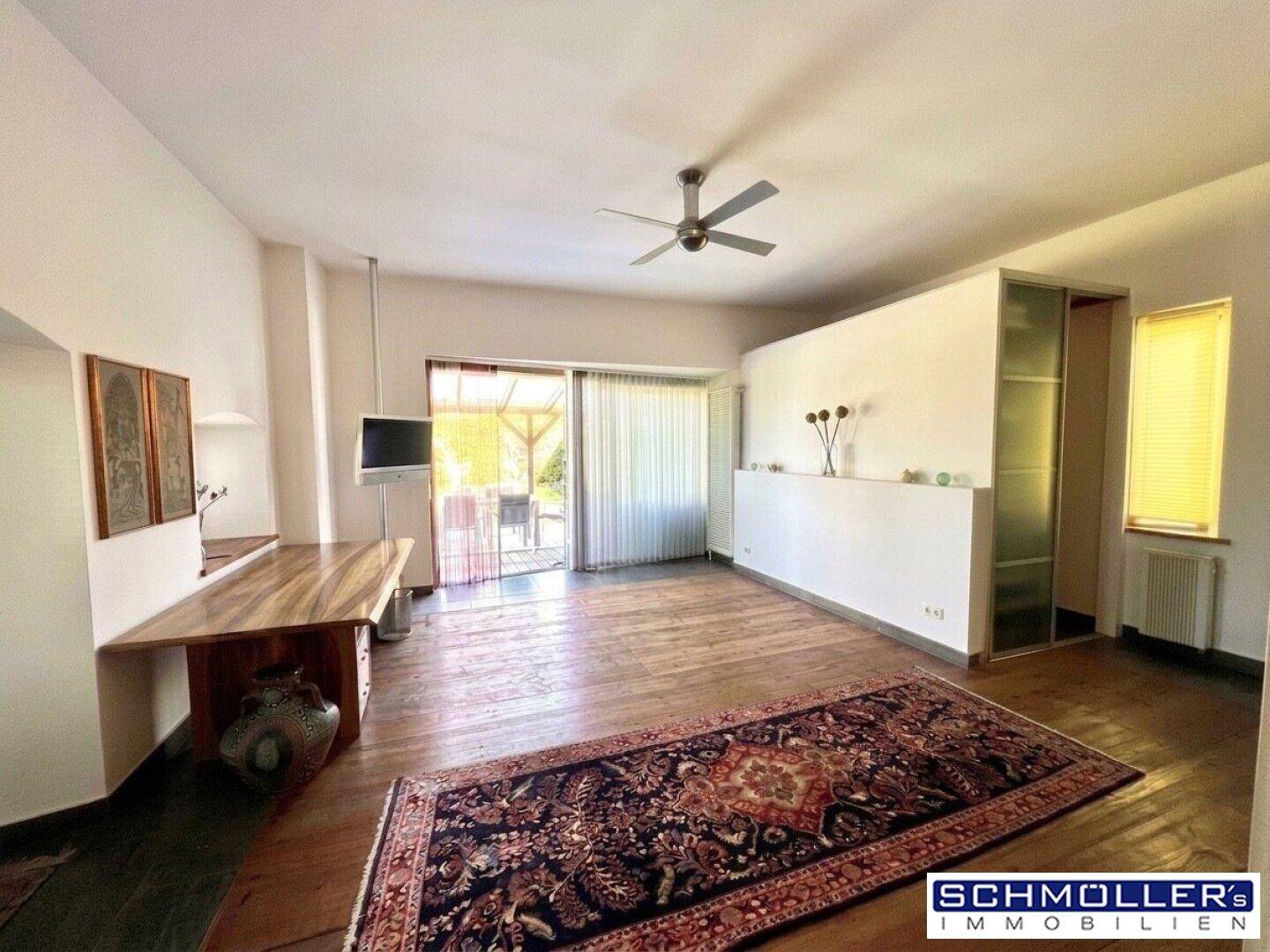 Heller Wohnraum mit Holzboden, Deckenventilator und Zugang zu einer Außenterrasse.