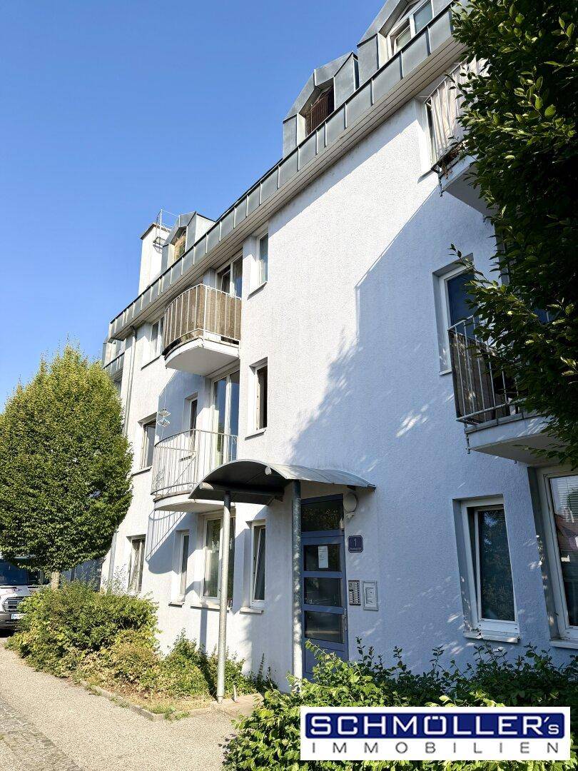 Mehrfamilienhaus mit weißer Fassade und mehreren Balkonen unter blauem Himmel.