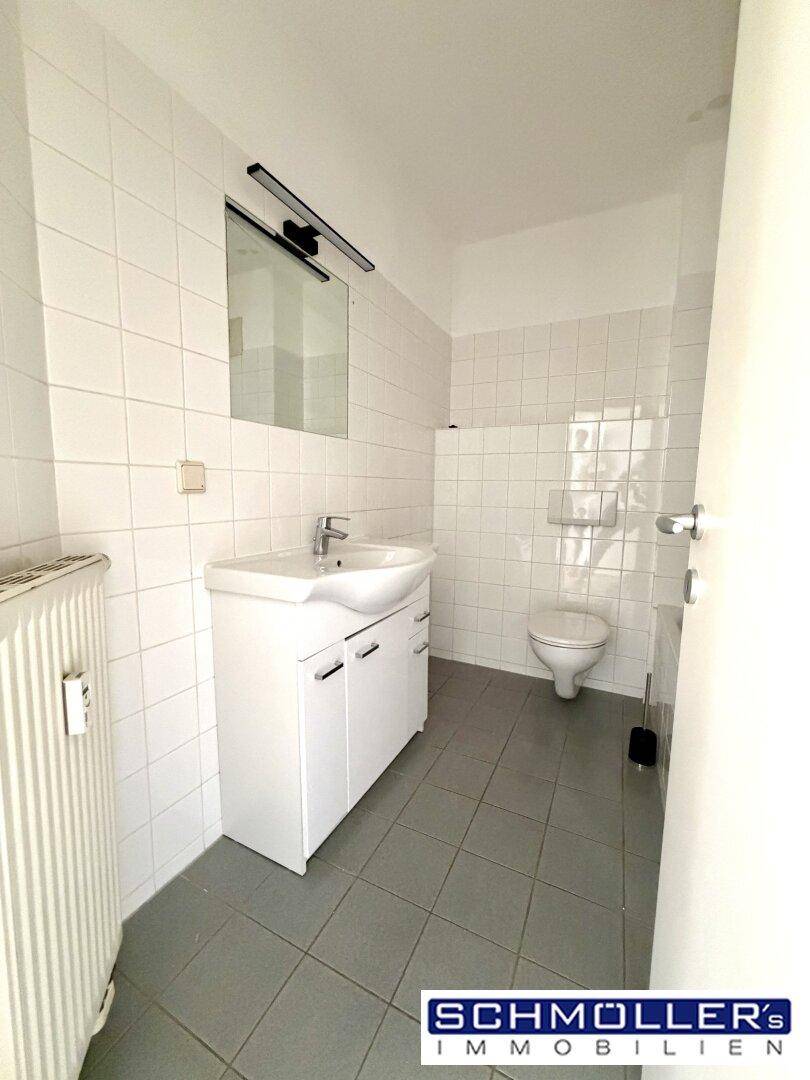 Badezimmer mit weißen Fliesen, Waschtisch und Toilette.