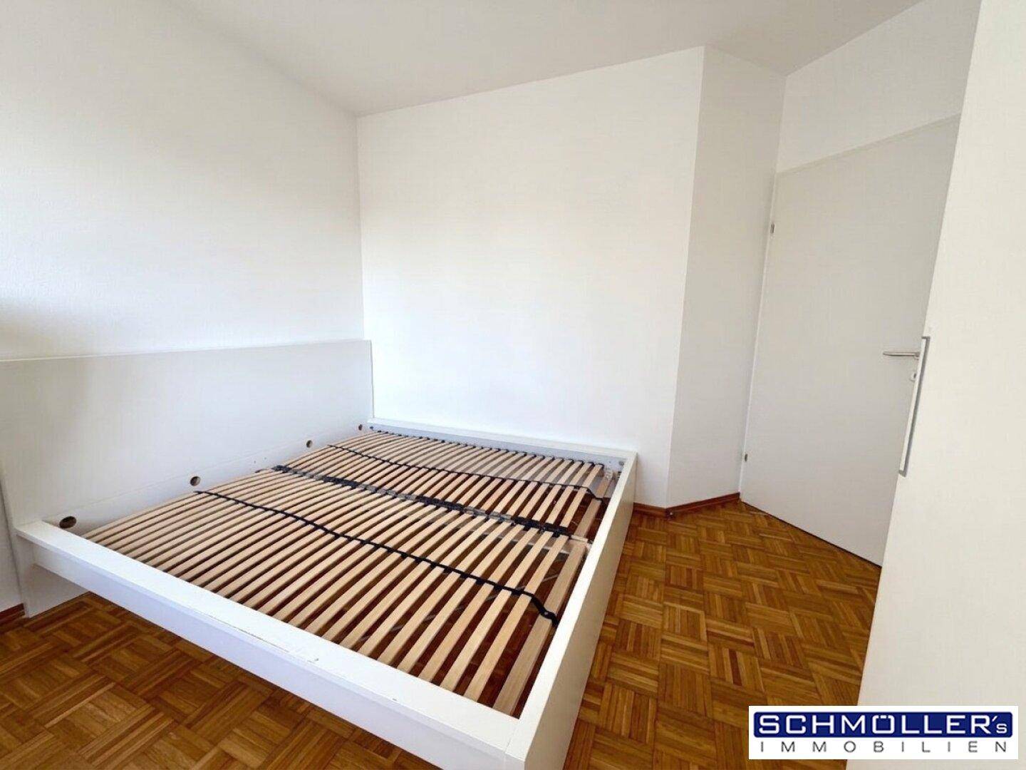 Schlafzimmer mit hellem Parkettboden und weißem Bettrahmen.