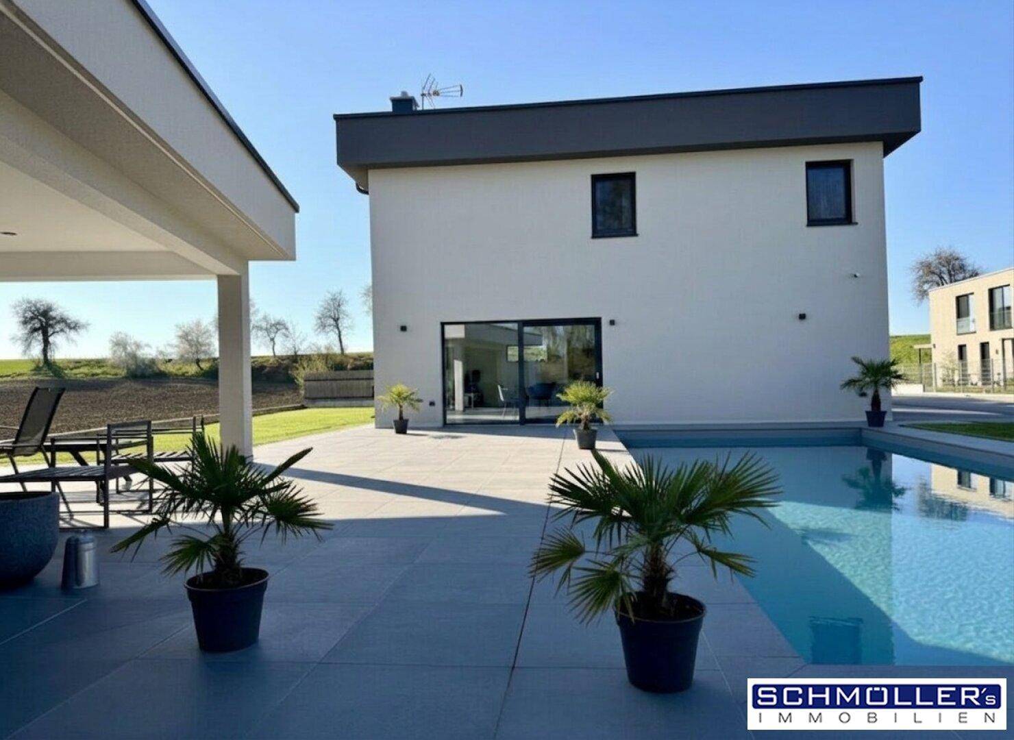 Rückseite des modernen Hauses mit Swimmingpool, überdachter Terrasse und weitem Blick ins Grüne.