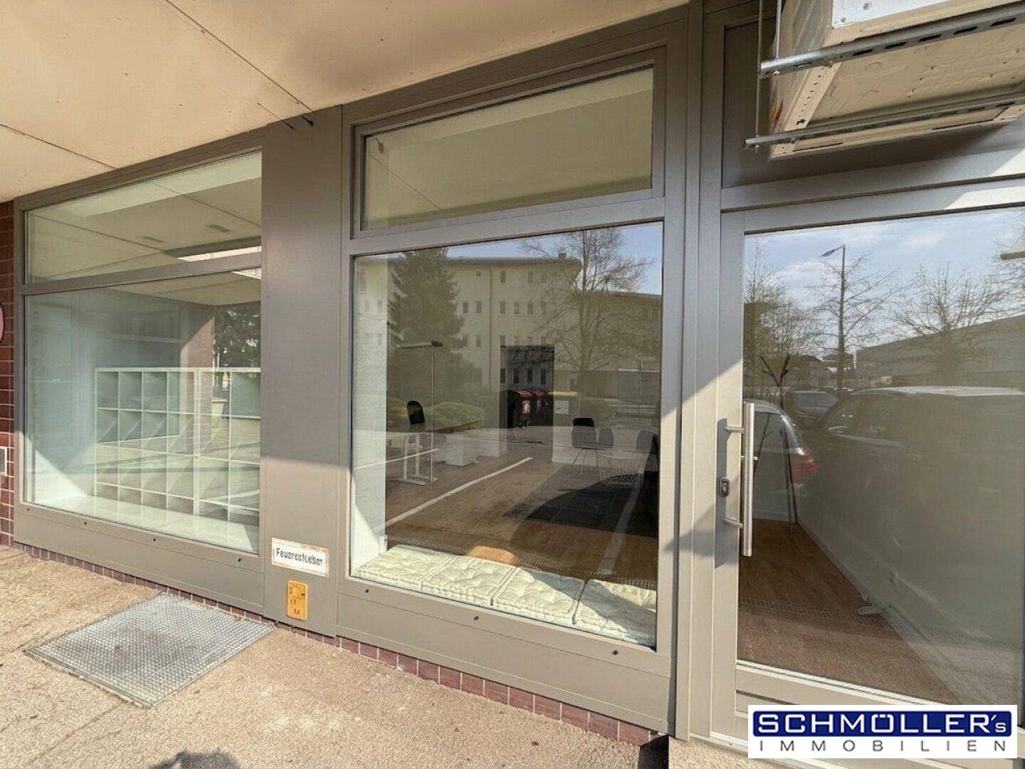 Außenansicht eines Geschäftsgebäudes mit großen Schaufenstern und Eingangstür, die den Innenraum zeigen.