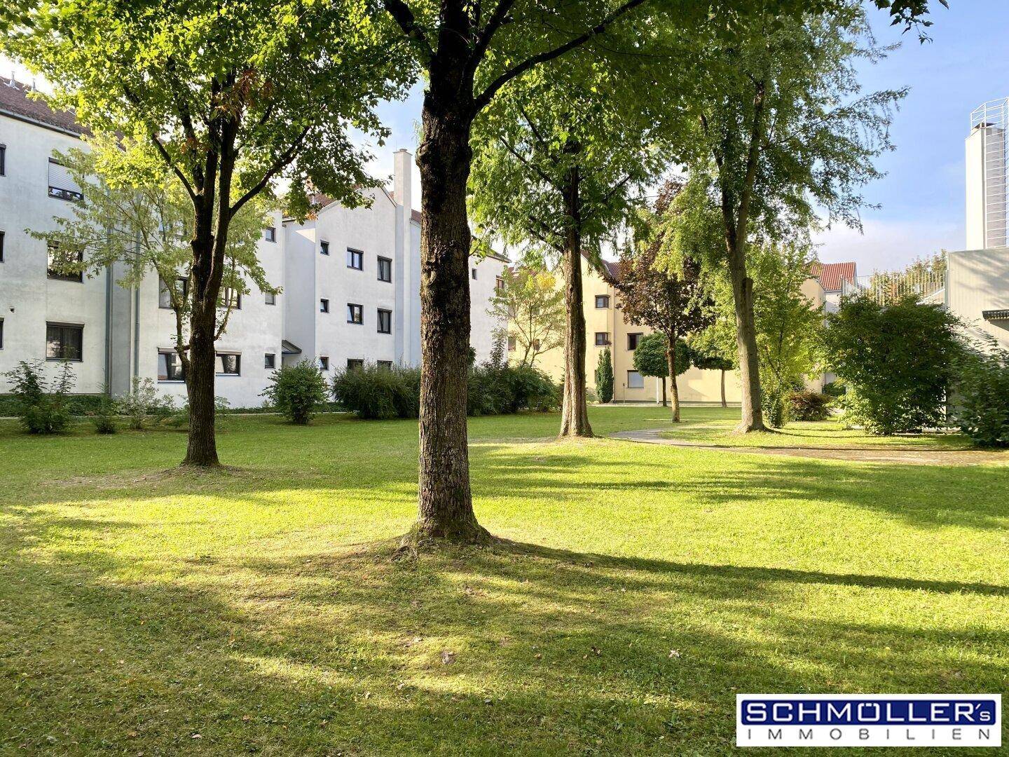 Gepflegte Grünfläche mit Bäumen und Rasen, umgeben von Wohngebäuden.