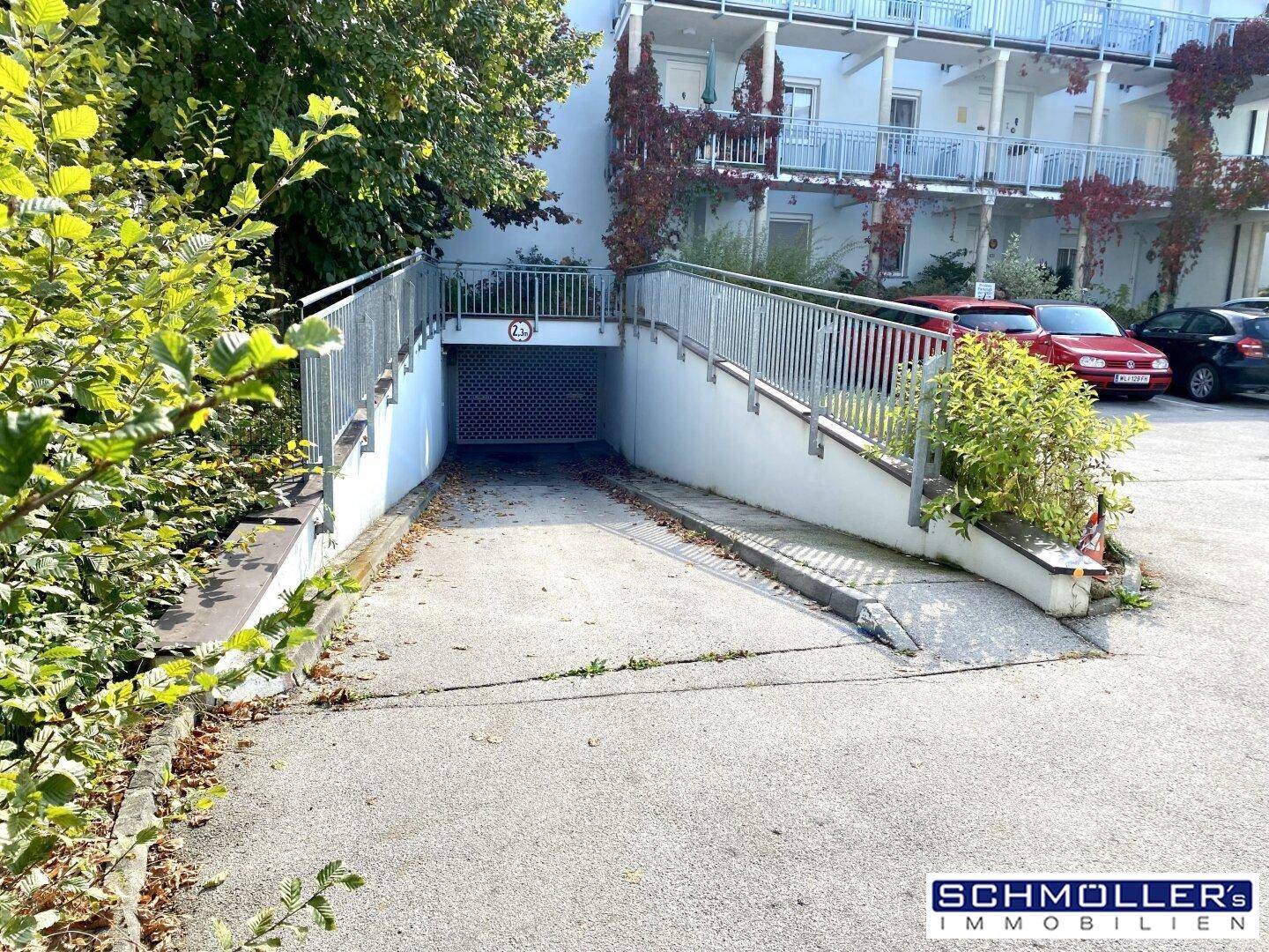 Zufahrt zu einer Tiefgarage mit Rampe und umgebender Bepflanzung.