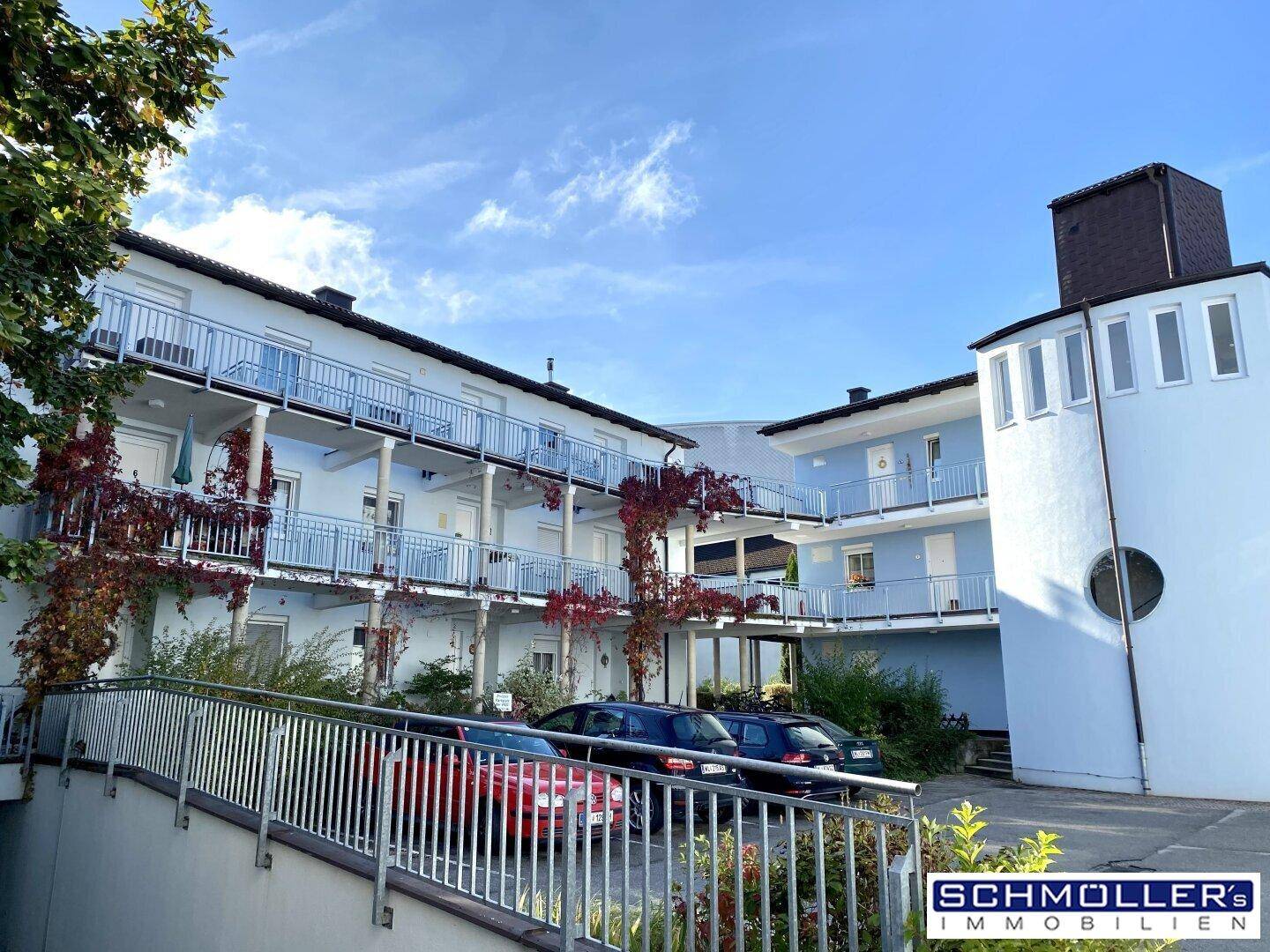 Wohngebäude mit mehreren Balkonen und Parkplätzen im Freien unter blauem Himmel.