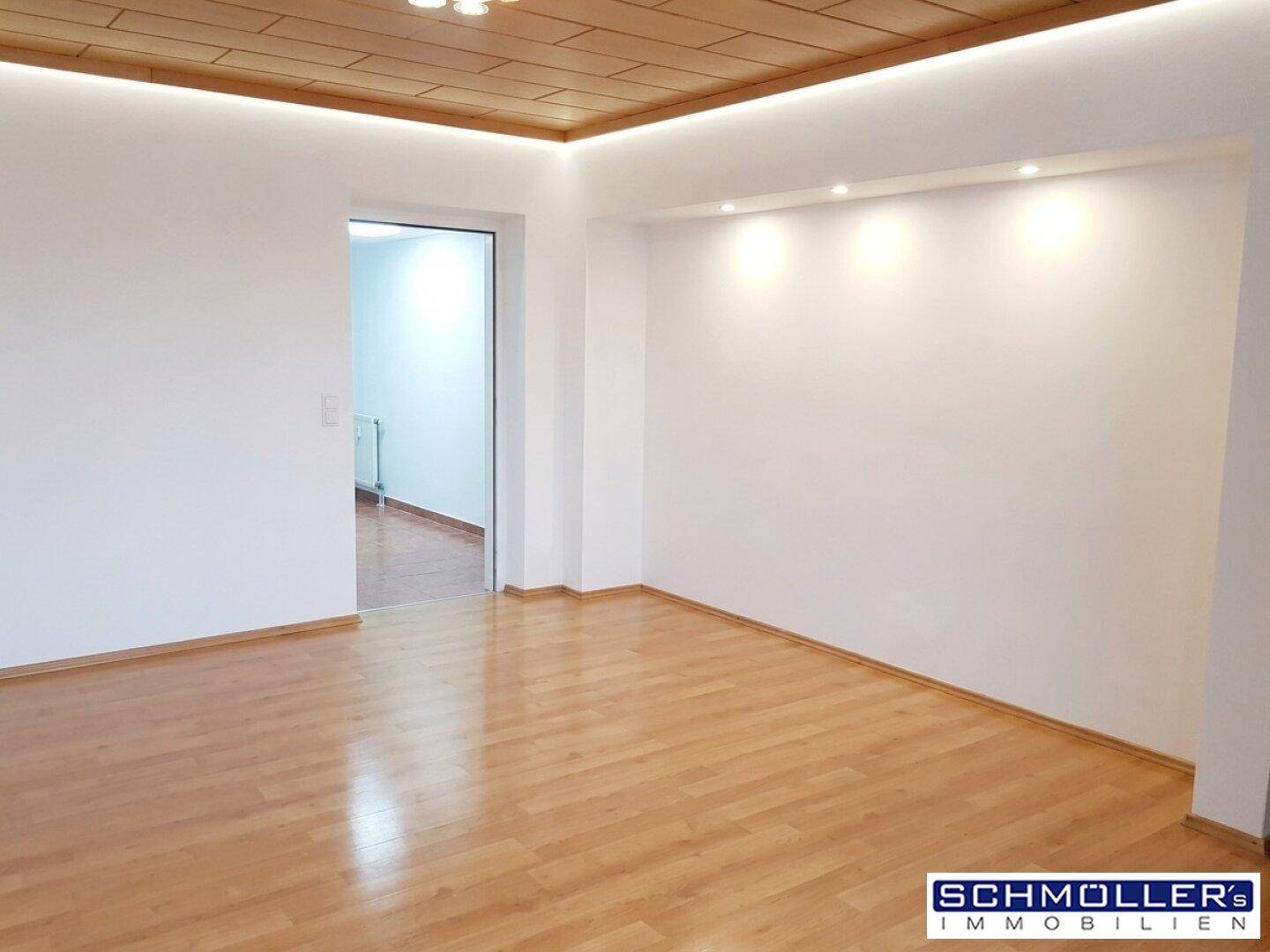 Geräumiges Wohnzimmer mit hellem Laminatboden und indirekter Deckenbeleuchtung, frisch gestrichen.