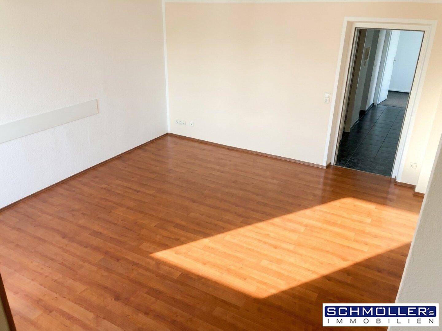 Leeres Zimmer mit hellem Laminatboden und viel Tageslicht, bereit zur individuellen Gestaltung.